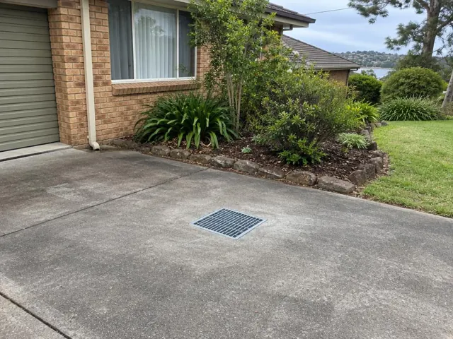 Concrete driveway with a seated stormwater grate beside a brick house and garden in Gymea Bay