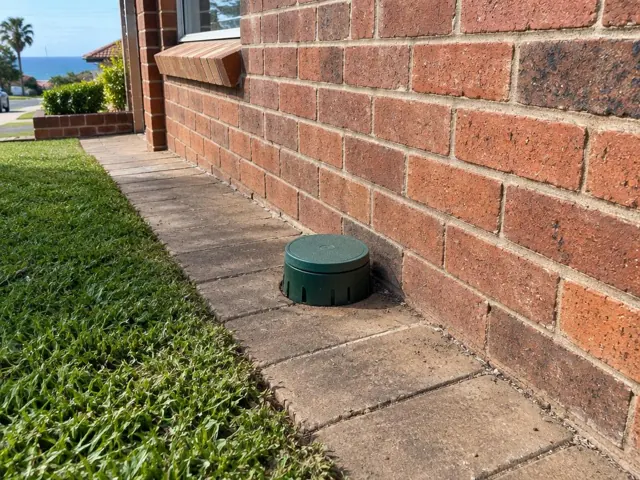 Capped sewer inspection opening beside a brick house and paved path in Cronulla